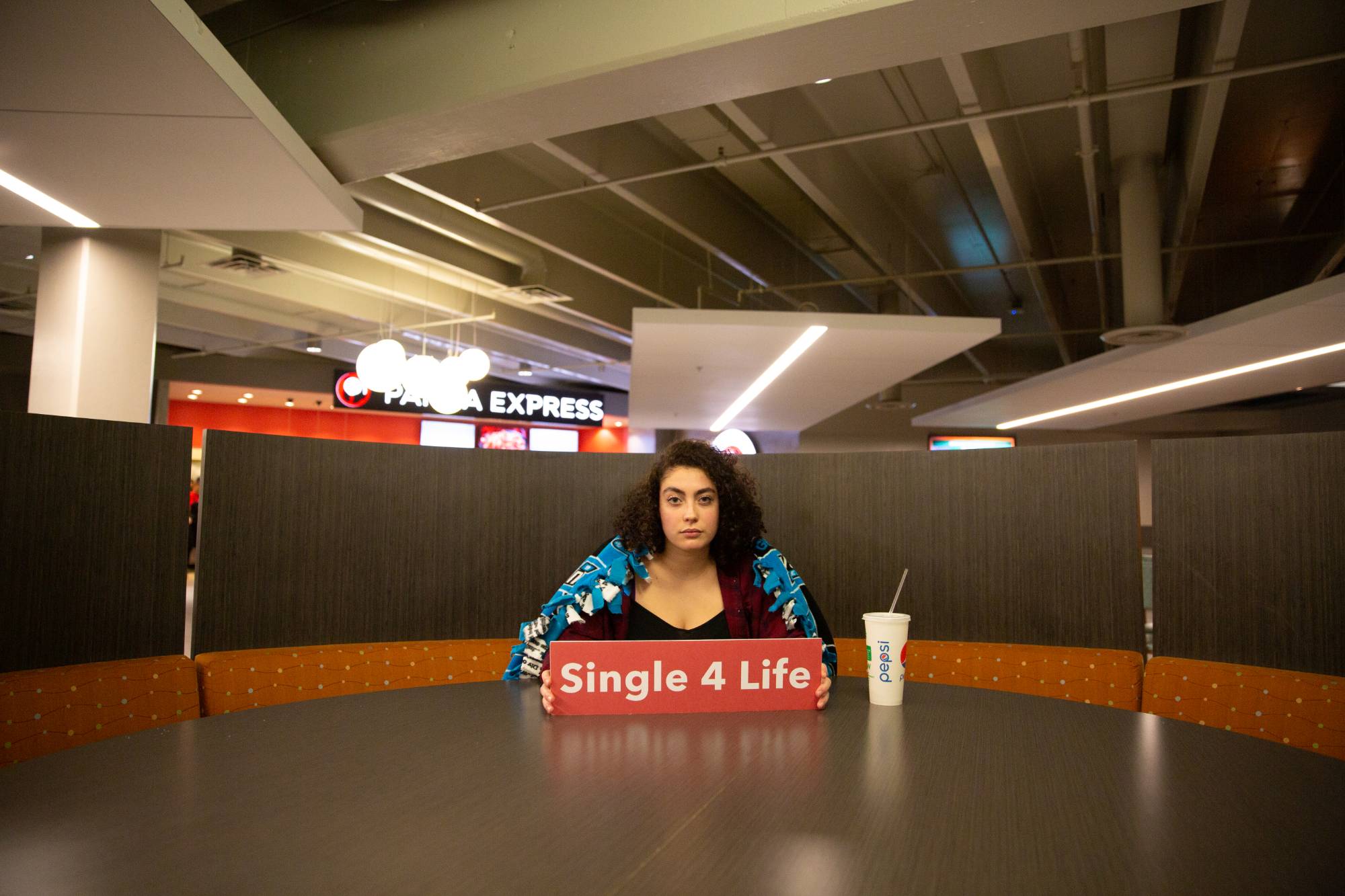 Student sitting alone at a table with a sign labeled "Single 4 life"